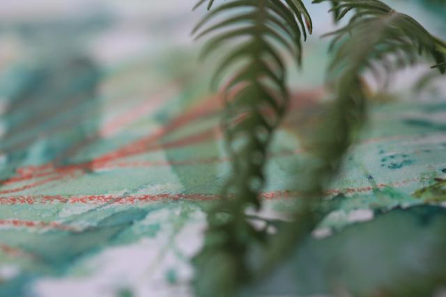 A close-up of some pastel and paint marks, obscured by a fern leaf in the foreground