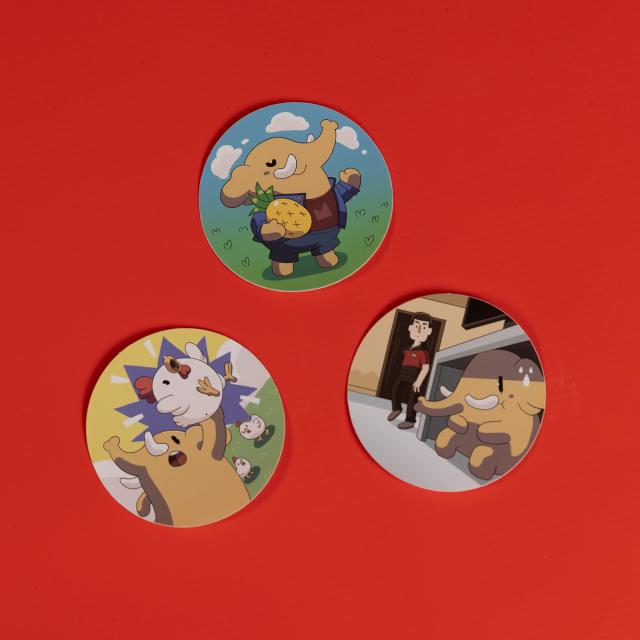 Three stickers on a flat surface. One sticker features an elephant dressed in a jean outfit and holding a pineapple. Another features an elephant hiding under a table while a man in a red space outfit is looking for him. The last one features an elephant holding a chicken, with more chickens in the background.