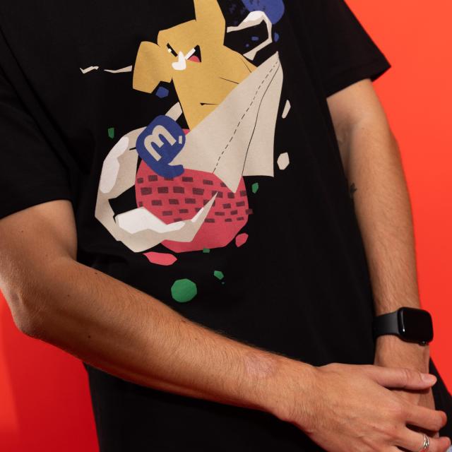 The new Mastodon t-shirt, 100% cotton. It is a black t-shirt with a large screen printed design on the front, featuring a cute elephant riding a paper airplane, with colorful planets behind it.