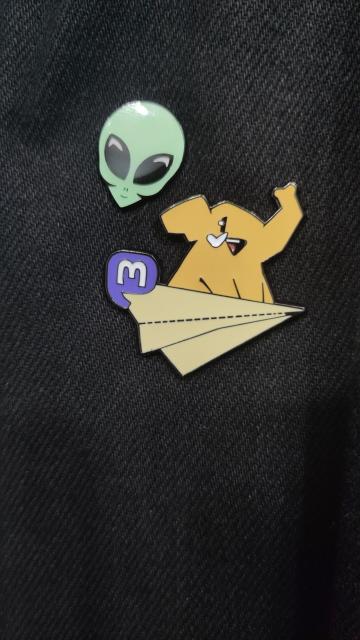 Masto pin badge next to a grey alien 👽 pin