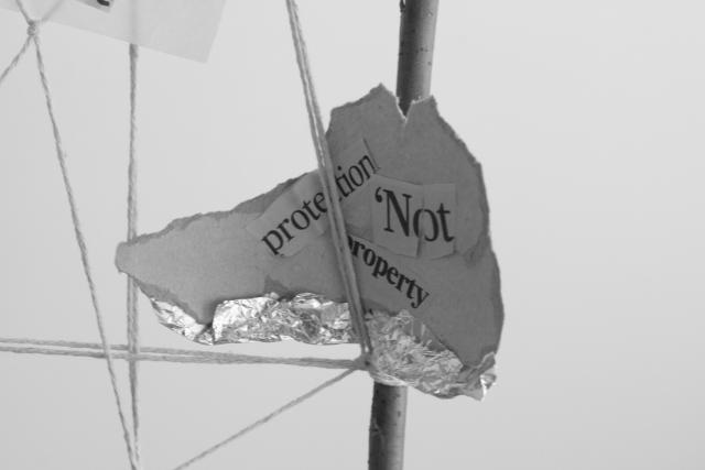 A crude cardboard shape with the words 'Protection not property' stuck on and tinfoil on the bottom. The shape is held into a cobweb-like form.