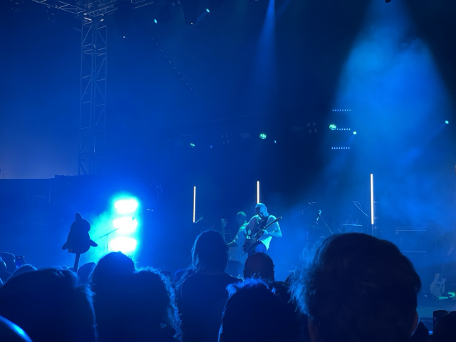Tented festival stage covered in blue light, three men playing musical instruments