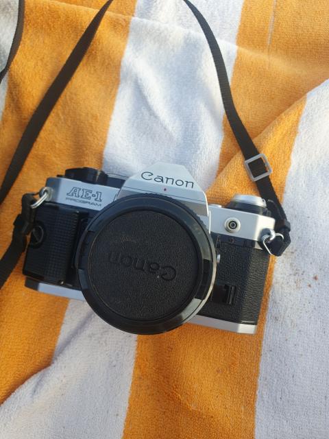 Silver and black Canon AE-1 Program SLR film camera on a white and orange beach towel. Lens cap is on.