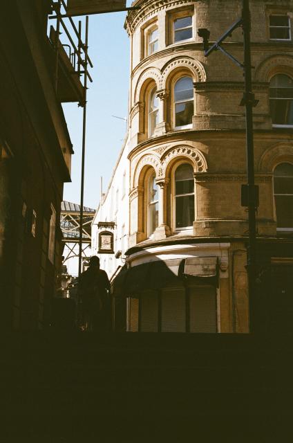A sunlit building with a round corner next to an alley with string lights