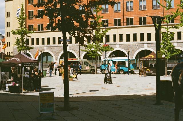 A food court illuminated by a pool of harsh midday light. The food trucks are colorful.