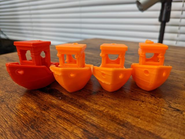 A set of four Benchies (a boat model that is used as a benchmark in 3D printing). One of them (on the left) is red, and the others are orange