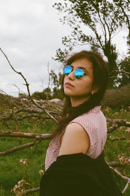 Beautiful woman with long black hair, wearing mirrored sunglasses that brightly reflect the sky, looking over her exposed shoulder as her hoodie is slightly lowered