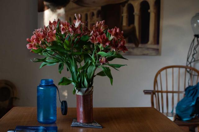 A vase of flowers and a blue bottle on a table top.