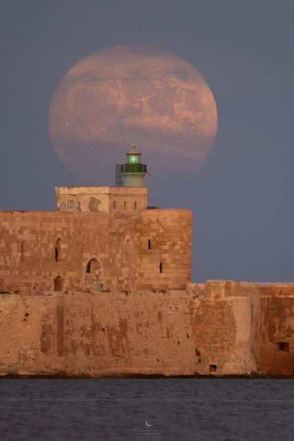 A large Moon is seen behind a historic stone structure.