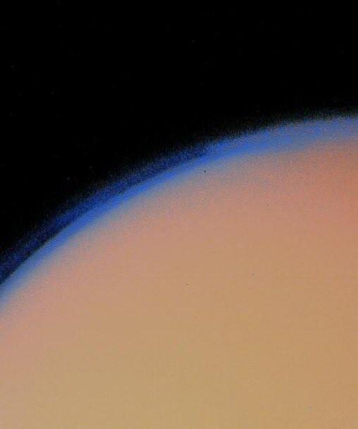 A color photo of Titan sent back by Voyager 1. The hazy blue limn of an atmosphere is visible; the moon itself is a featureless yellow-orange.
