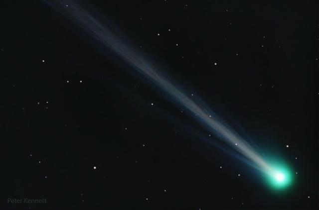 A comet is shown with its green coma on the bottom right and a long and structured ion tail flowing diagonally across the image toward the top left.