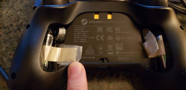 A steam controller is pictured with its back cover off and a ribbon with tape is wrapped around the battery to give it a handle.