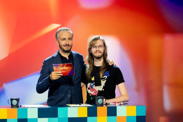Jan Böhmermann und Erik Uden stehen hinter einem Moderationspult im Studio von Lass dich überwachen und haben sich die Arme gegenseitig auf die Schulter gelegt.