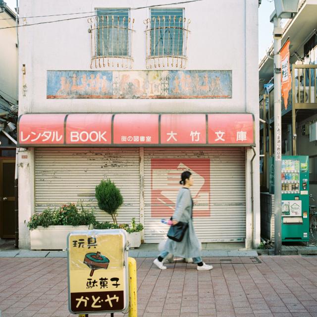 A woman passing an old building with faded painted advertisements in Kōenji, Tokyo, Japan.