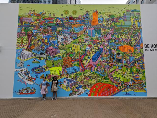Colourful mural of a cartoon of the Kobe area buildings, streets, bridges and port with Be Kobe written to a side.
2 kids are standing in front of the mural (which is about 25 feet tall by 30 feet wide, approx)