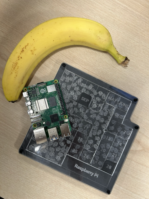 A daily month and date puzzle made from laser cut acrylic with a Pi 5 resting on it next to a banana for scale 