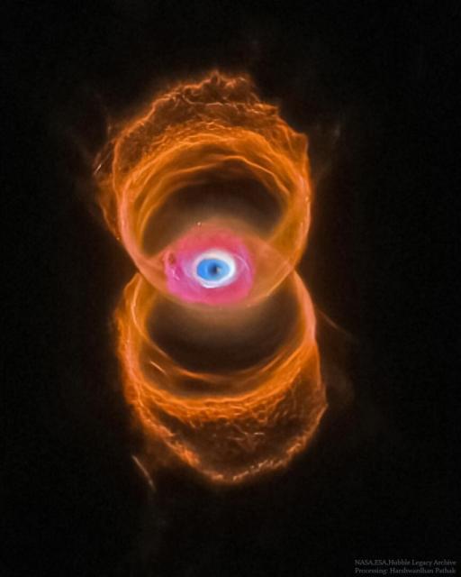 A vertical planetary nebula is shown in orange around the outside but with a blue glow in the center. The outside is shaped like a tilted hourglass, while the inside appears similar to an eye.