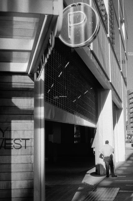 A worker takes a smoke break in the midst of numnerous intersecting shadows and vanishing lines.