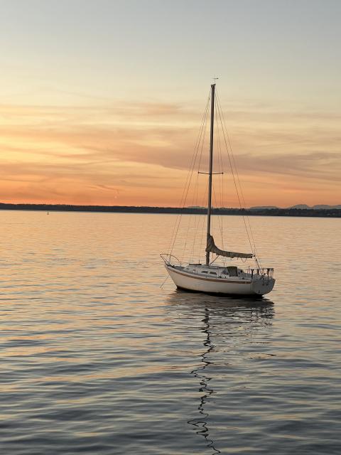 A single sailboat anchored at sea on calm waters where the sun sets behind the San Juan Islands.