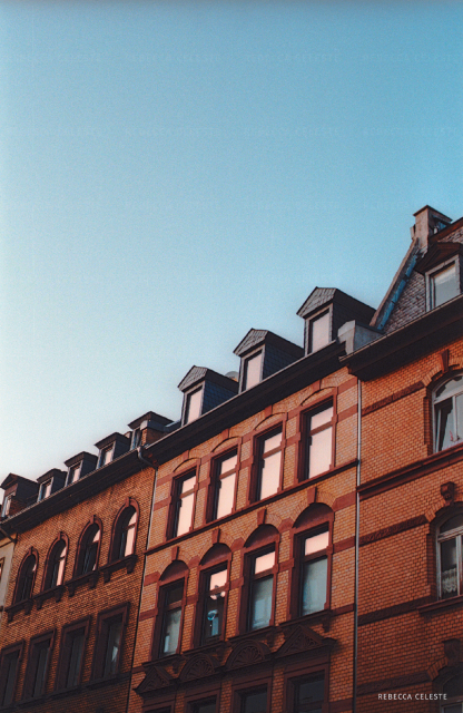 A blue cloudless sky and a red-brown building. The windows reflecting a sunset.