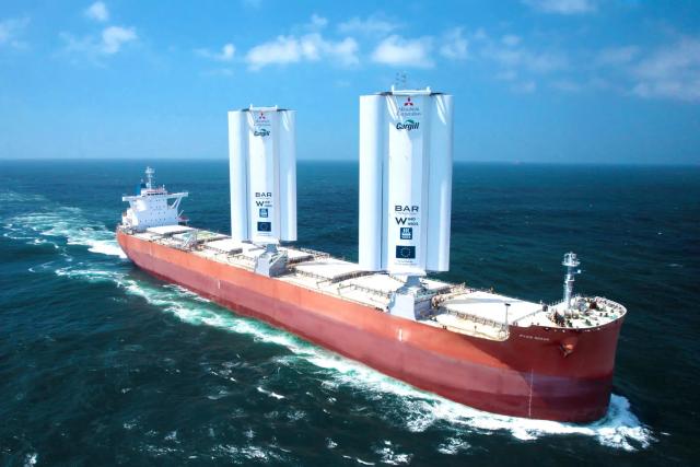 A photograph of a cargo ship with a pair of tall, white things protruding from the top. They are sails, but they look more like grain elevators.