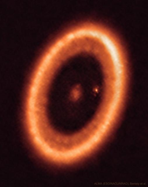 An orange elliptical ring is shown that is a disk of gas and dust around the star PDS 70. In the center of the disk is a fuzzy spot and near the inner right edge of the disk is another fuzzy spot.