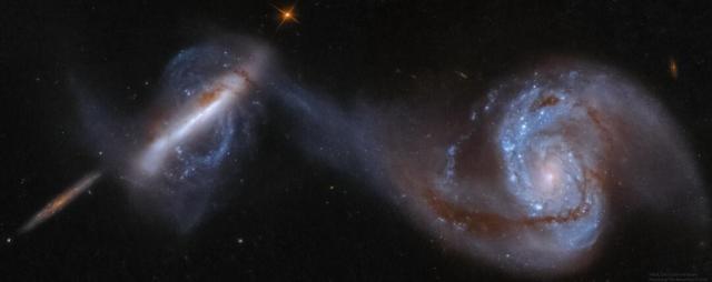 Three large galaxies are shown, the rightmost two in collision. The galaxy on the far right is a large spiral galaxy with one arm connected to an unusual polar galaxy on the left. The smaller galaxy on the far left is thought to be far in the background.