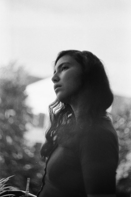 A black and white photo of a woman with dark hair, looking thoughtfully to the side. In the background, there is bokeh that becomes swirlier towards the edge