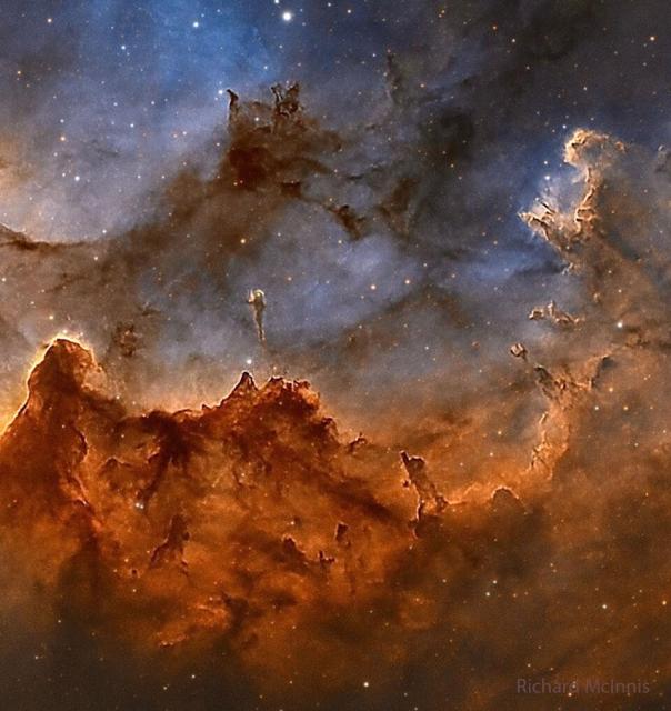 The center of the Wizard Nebula is shown featuring gas glowing in red and dust reflecting in blue. Dark dust pillars are seen throughout the image.