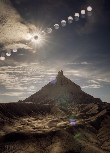 A sequence of Sun and Moon images are shown behind a scenic foreground that features the large Factory Butte. The foreground was taken during the maximum part of the annular eclipse and seems somehow oddly lit.