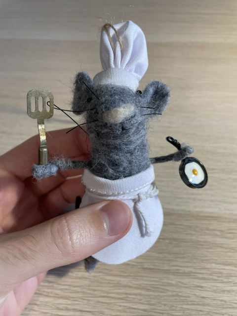 A felt ornament of a mouse dressed as a chef, holding a cooking spatula in one hand and a frying pan with a fried egg in the other.