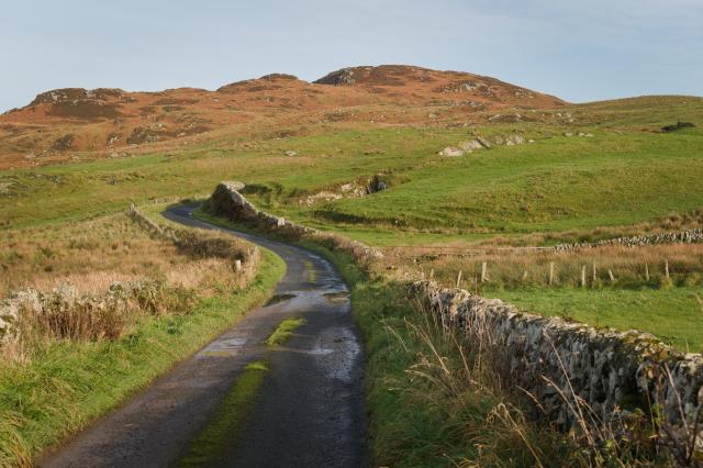 a winding single track road leading towards a small hill
