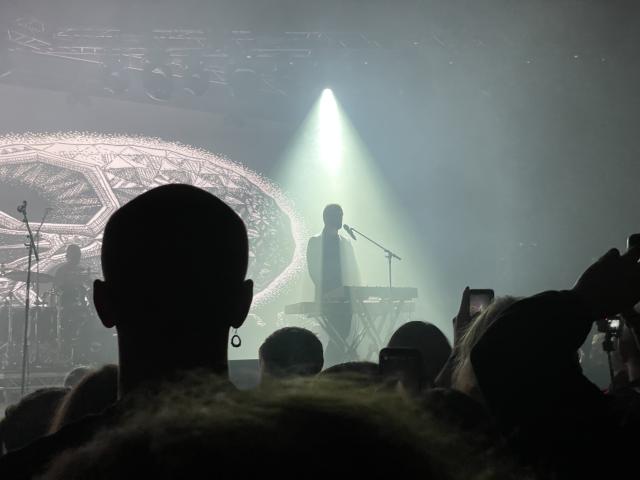 Lead vocalist on stage in front of a microphone and keyboard illuminated by white light