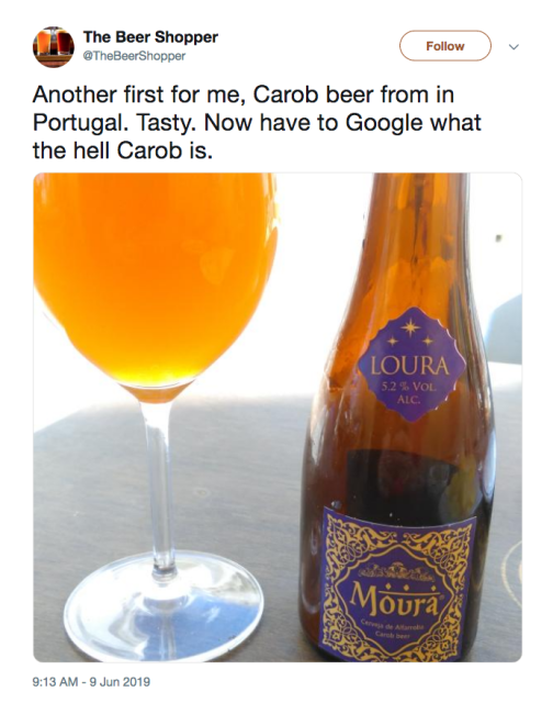 Tweet by @TheBeerShopper with phto of an amber-colored liquid in a red wine glass next to a brown beer bottle with purple labels with gold text and decoration in an Islamic art-influenced style. Label says "Loura 3.2% vol alc. Moura cerveja de alfarroba. Carob beer."  Both glass and bottle are on a white tablecloth and backlit in a clearly sunny vacation spot. Text of tweet says "Another first for me, Carob beer from in Portugal. Tasty. Now have to Google what the hell Carob is."