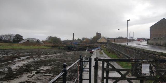 Walking into town from Workington Harbour.

The harbour is full of low tide mud. A harbourside path stretches towards a church on the horizon.

It is a little wet.