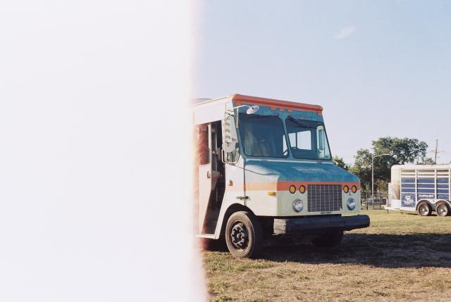 Color film photo of the front half of a white/blue/orange food truck, the half is consumed by the light exposure from loading the film.