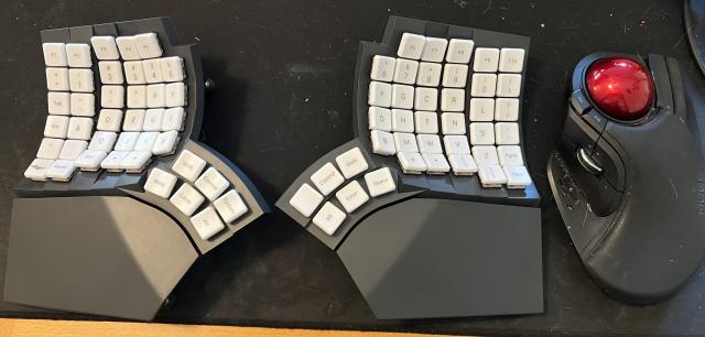 A black split ergonomic keyboard with white keys, with a large trackball mouse to the right