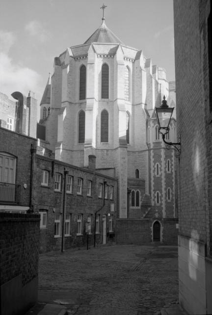 Black and white film image of Manchester Mews in London. Cobbled yard with brick buildings and a white ambulatory outer wall of a nearby Cathedral.