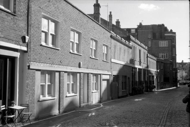 Black and white film image of Beaumont Mews, cobbled Road and lined with brick buildings.