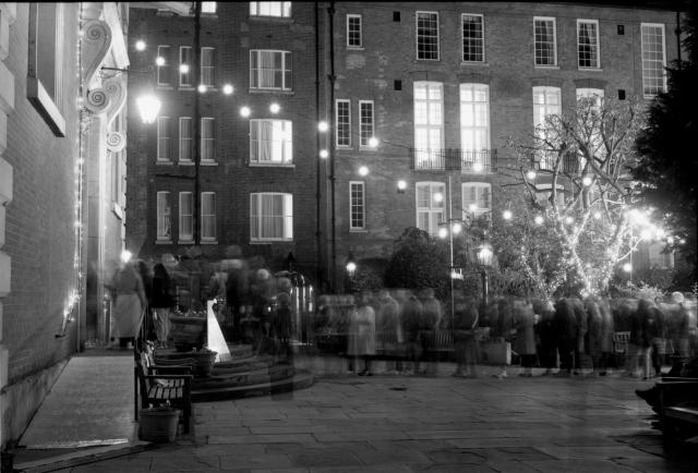 Black and white film image taken at night of the rear of St Paul's Church in Covent Garden. There is a queue of people that appear blurred due to the long exposure time while they moved slowly along.