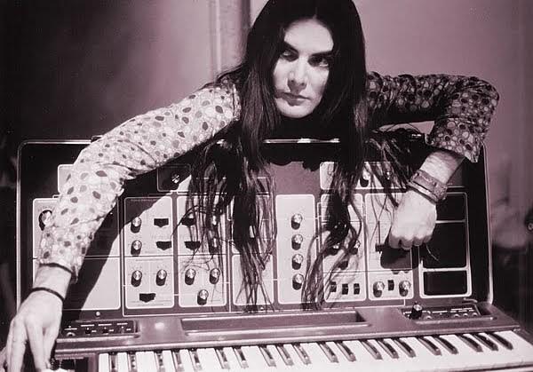 Black and White photo of Wendy Carlos, looking moody and magnificent, leaning over the back of a Moog (?) Modular synthesiser, her long dark hair hanging over. Queen 👑