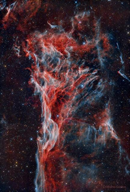 A nebula consisting of blue and red wisps starts thin at the image bottom but expands into a triangle at the image top.