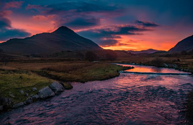 Sunrise over a flowing river. Munro in the background.