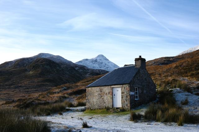 photo of a small bothy, a snow covered peak rising behind