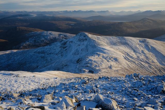 view from above to a lower snowy peak, visibility is excellent and you can see off to other mountains far in the distance