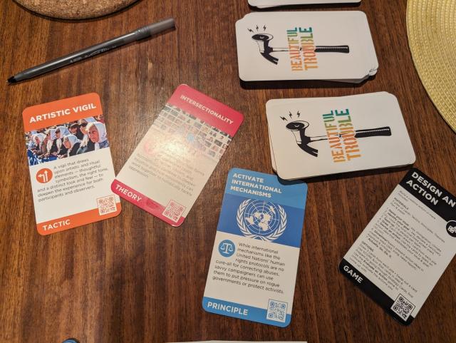 Beautiful Trouble cards, "Artistic Vigil", "Intersectionality" and "Activate International Mechanisms" on a table.