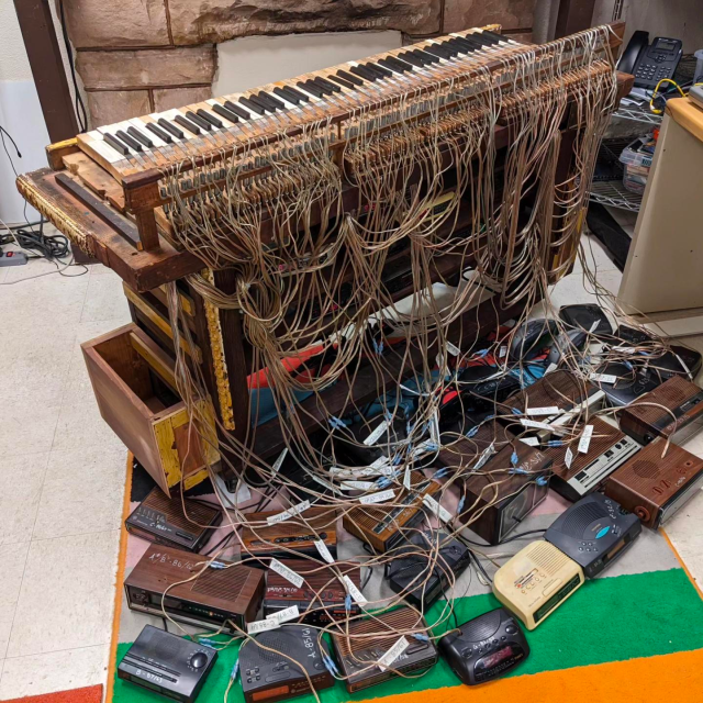 Emily Francisco's Trans-Harmonium - a skeleton of a piano with each key wired to a different clock radio