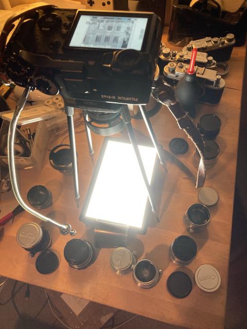 A full suite of LTM and Contax 50mm lenses arranged around a light box and a BOOWU copy stand.