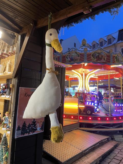 A plush goose hanging off a kiosk by the neck at a Christmas market