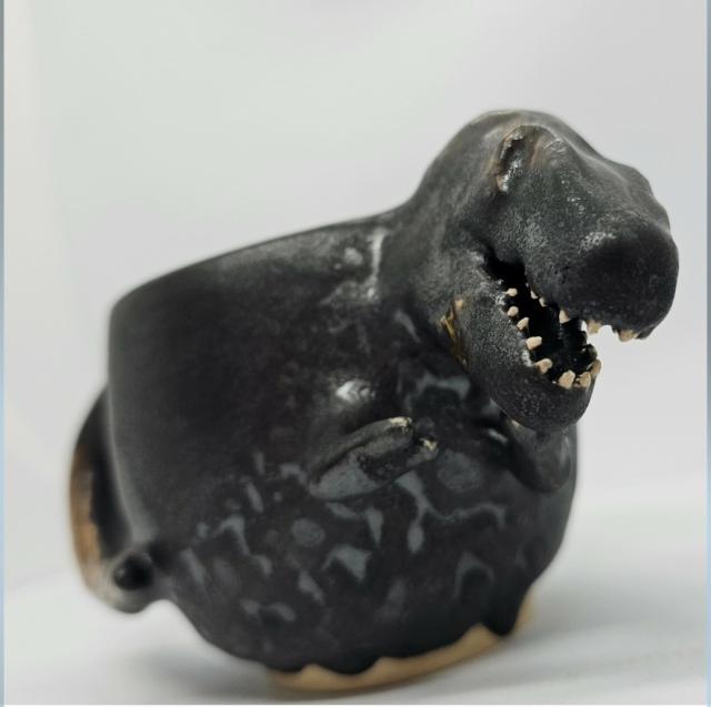 Black t-rex mug, with white teeth looking down on the camera 